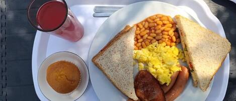 A tray with toast, beans, sausages, scrambled eggs, and a glass of red drink.