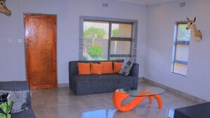 Una sala de estar con un sofá gris, cojines naranjas, una mesa de centro de vidrio y una cabeza de venado montada.