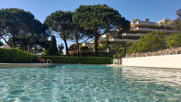 Une piscine aux eaux cristallines, entourée d’une végétation luxuriante, et un immeuble à plusieurs étages doté de balcons.