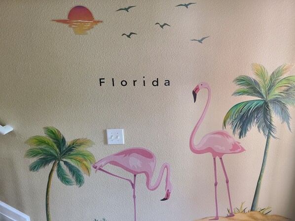 Un mur orné d’une fresque représentant un flamant rose, des palmiers et des oiseaux, avec le mot « Floride » écrit au-dessus.