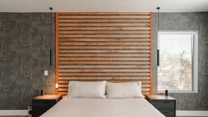 A modern bedroom with a wooden slat headboard, a large bed with a beige quilt, two bedside tables, and a window with blinds. - Modern Luxury! Only 10 min. to AZ Athletic Grounds & A+ Dining Shopping! (Mesa)