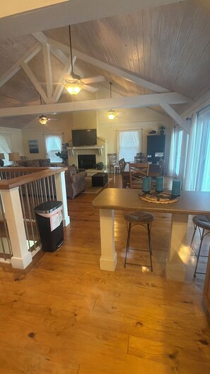 A spacious living area with a high ceiling, wooden beams, a fireplace, and a dining area with a bar.
