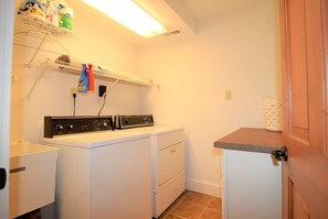 A laundry room with a front-loading washer and dryer, shelves with cleaning supplies, and a countertop with a basket. - A beautiful piece of Heaven on the waterfront (scottsboro)