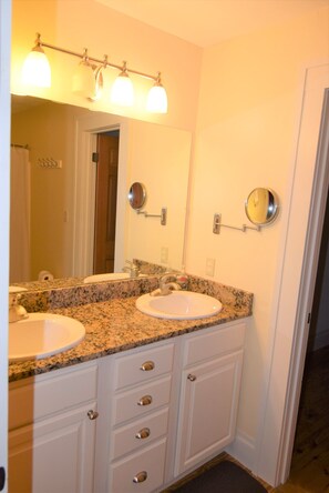Une salle de bain avec deux lavabos, un meuble-lavabo avec des tiroirs, un miroir et un luminaire placé au-dessus du miroir.