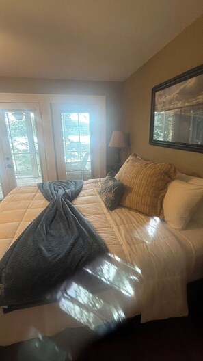 A hotel room with a bed, a window with blinds, a lamp, and a painting on the wall.
