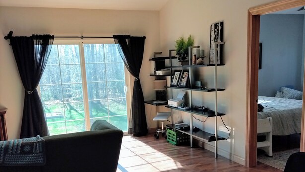 A spacious living room with a large window, wooden flooring, a black sofa, a black armchair, and a bookshelf. - Spacious home with EV charging station two miles from Big Bay Town Park. (La Pointe)