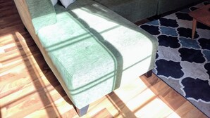 A living room with a green sofa, a patterned rug, and wooden flooring. - Spacious home with EV charging station two miles from Big Bay Town Park. (La Pointe)