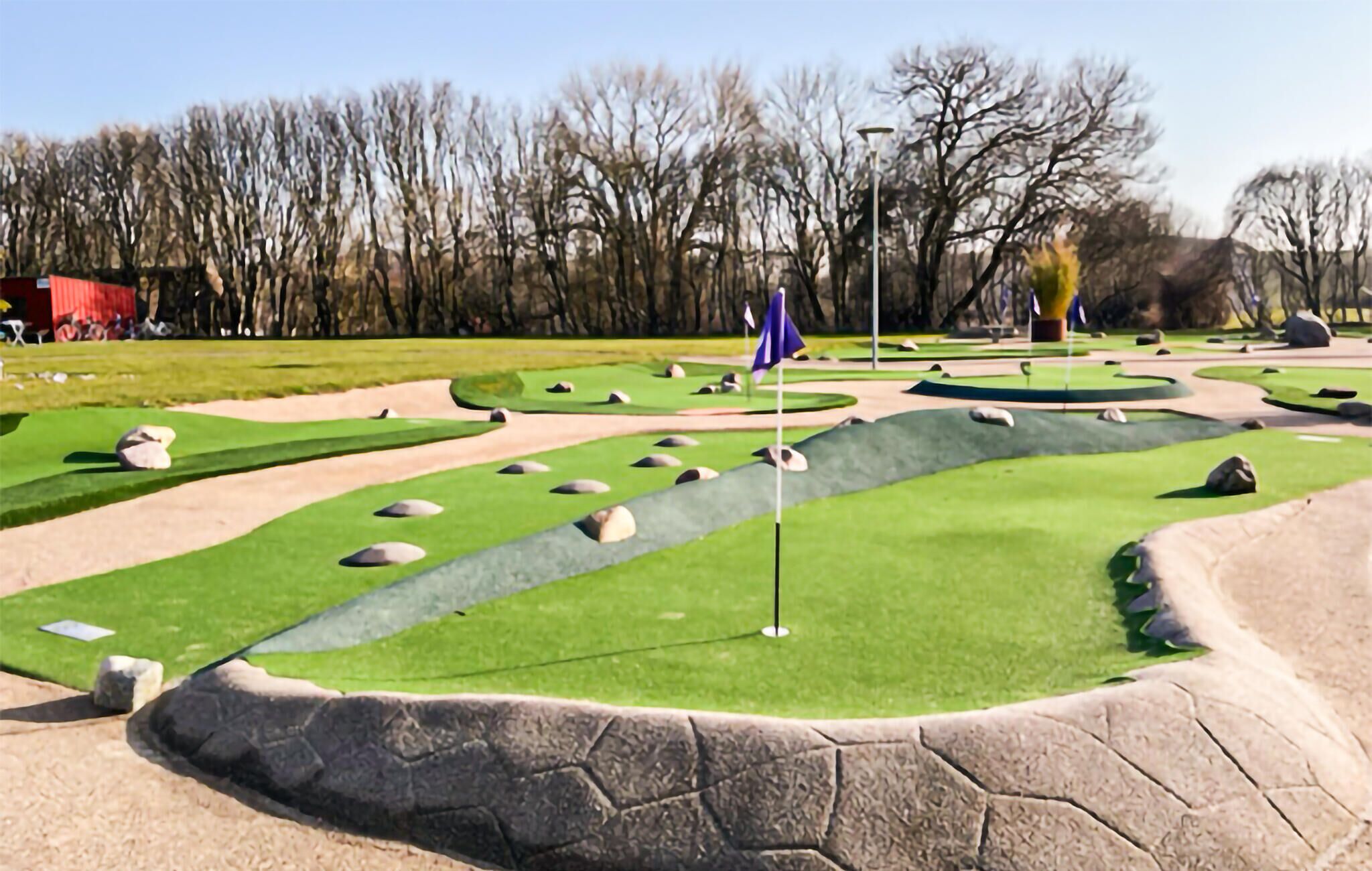 Un parcours de minigolf avec des obstacles de sable, un drapeau et un mât.