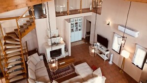 A spacious loft-style living area with a wooden staircase, a fireplace, a TV, and a hanging light fixture.