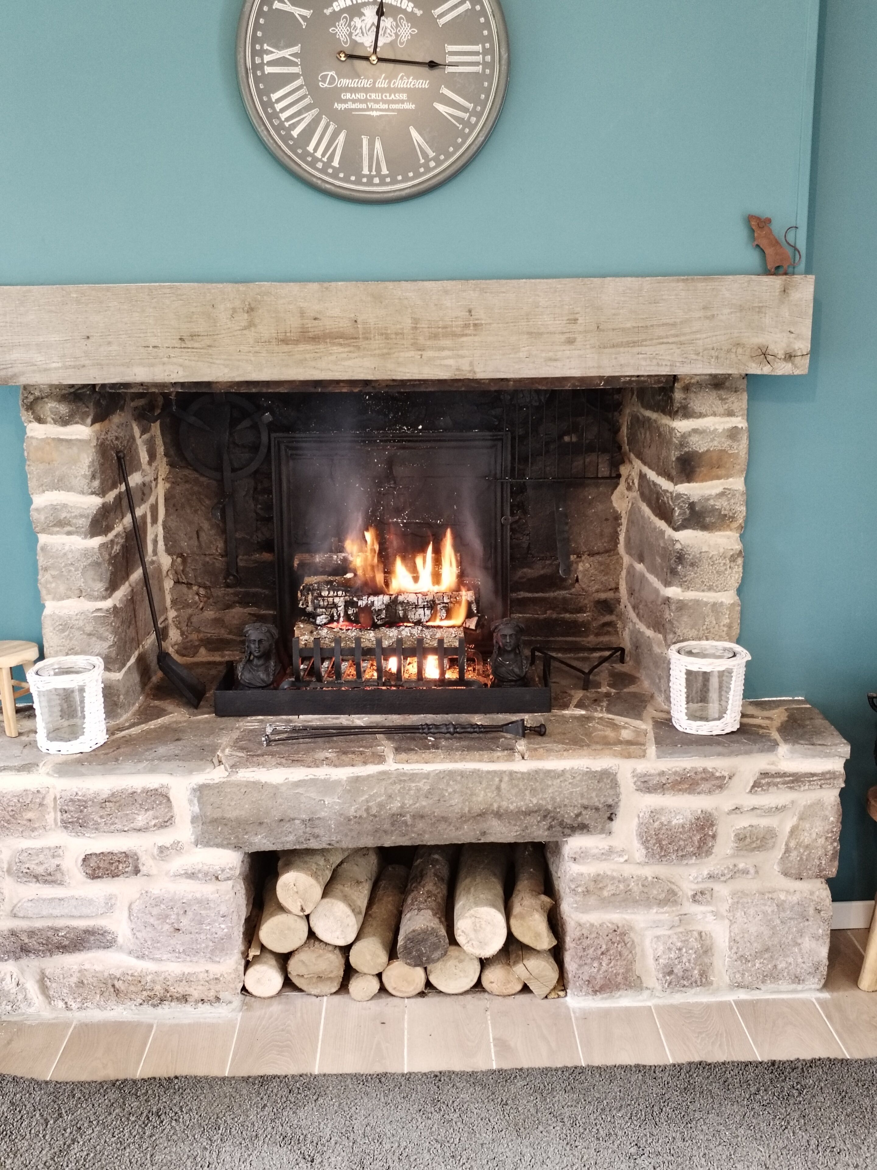 Una chimenea de piedra con fuego, un reloj encima y dos velas a cada lado.