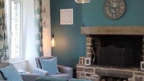 Un salon chaleureux avec une cheminée en pierre, une horloge et un luminaire suspendu.