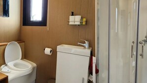 A modern bathroom with a toilet, sink, and glass-enclosed shower. - Escape to a Rustic Modern Farm Cabin with Outdoor Bath (Waitoki)