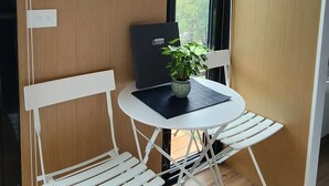 A small room with a wooden wardrobe, a black laptop on a white table, a potted plant, and a window with a view of greenery. - Escape to a Rustic Modern Farm Cabin with Outdoor Bath (Waitoki)