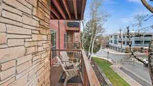 Une terrasse en bois avec deux fauteuils Adirondack, un mur en pierre et une vue sur une rue et des immeubles.