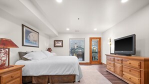 Une chambre à coucher comprenant un lit, une télévision, une commode et une porte donnant sur un balcon.