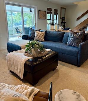 A living room with a blue sofa, a coffee table with a plant, a fireplace, and a view of the outdoors. - Unmatched Lakefront 3 bed/3 bath, 2 King Home of HH! Private Dock w/ Slip (Lake Ozark)