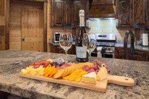 A wooden interior with a marble countertop displaying a charcuterie board, two glasses of wine, and a bottle of wine.