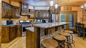 Una cocina de estilo rústico tipo cabaña, con armarios de madera, una isla de piedra y taburetes de bar.