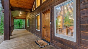 Una cabaña de madera con porche cubierto, ventanas amplias y felpudo de bienvenida.