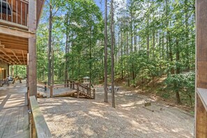 A wooden cabin with a covered deck and outdoor seating area, surrounded by a forest.