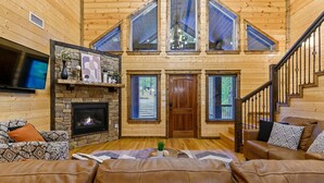 Interior acogedor de una cabaña de madera con chimenea, sofás de cuero y una escalera que sube a un nivel superior.