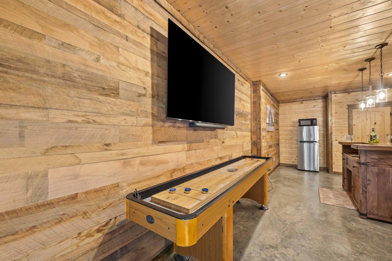 Un intérieur en bois avec un baby-foot, un téléviseur à écran plat et un réfrigérateur.