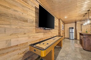 Un interior de madera con una mesa de fútbol de mesa, un televisor de pantalla plana y un refrigerador.