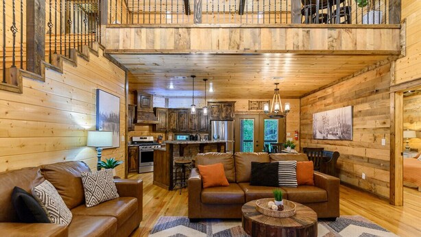 Interior acogedor de una cabaña con sala de estar, cocina y comedor, con paredes de madera y un balcón.