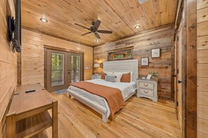 King bedroom with upholstered headboard, nightstands, ceiling fan and French doors.