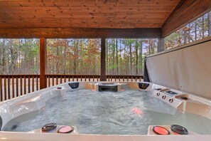 A hot tub with controls, surrounded by a wooden deck and a view of trees.