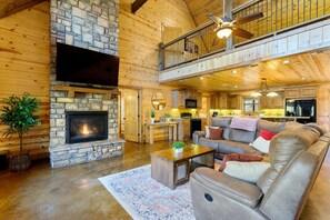 A spacious living area with a stone fireplace, a leather sofa, and a dining area with wooden cabinets.
