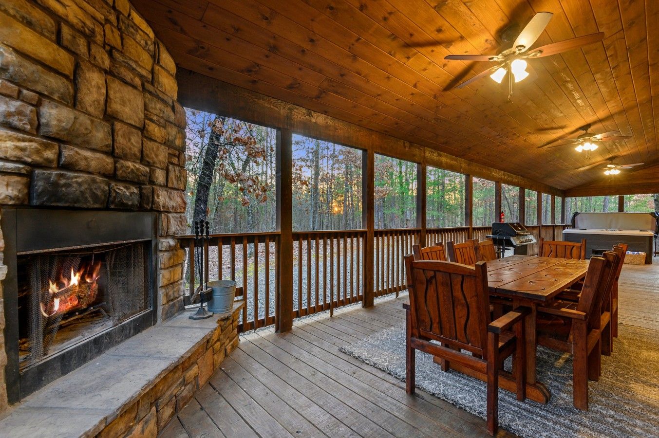 A covered outdoor area with a stone fireplace, wooden deck, and a dining table with chairs.