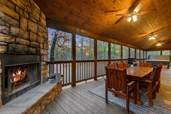 A covered outdoor area with a stone fireplace, wooden deck, and a dining table with chairs.
