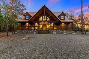 A log cabin with a stone foundation, a front porch, and a gravel driveway. - Wide Glide Lodge over 1 acre w Hot Tub Movie Room and Playset (Broken Bow)