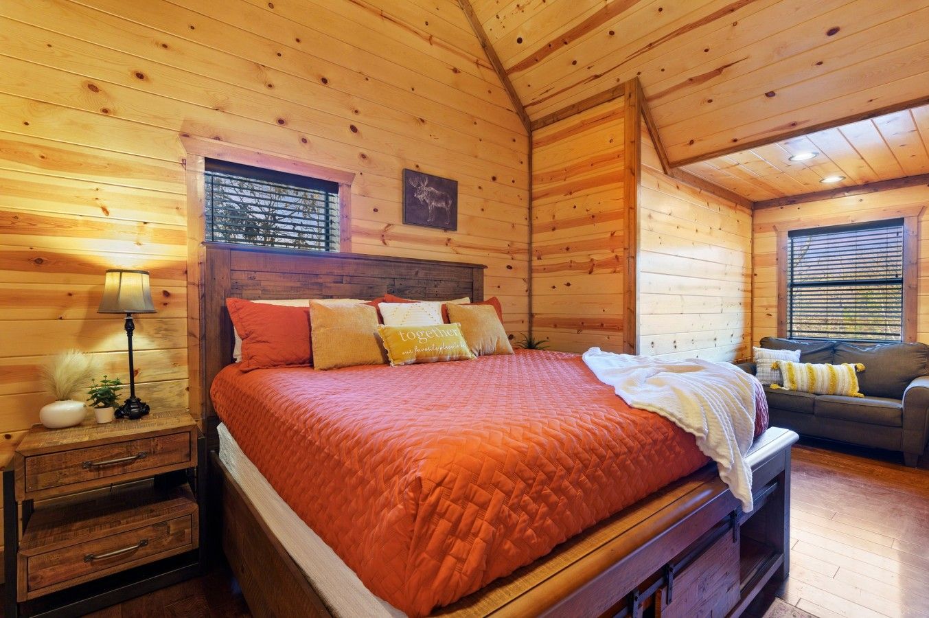Une chambre dans un chalet en bois, avec un lit, des tables de chevet, une lampe, une fenêtre et un canapé.