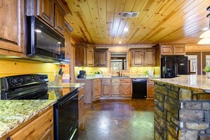 A kitchen with wooden cabinets, granite countertops, a black stove, and a stone backsplash.
