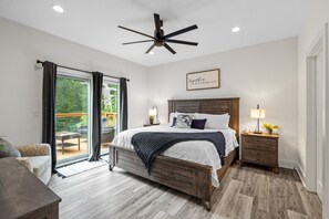 A bedroom with a bed, a ceiling fan, a nightstand, a dresser, a window with curtains, and a view of the outdoors. - Lux Chalet with Hot Tub Ride In/Out onto Back 40 Trails (Bella Vista)