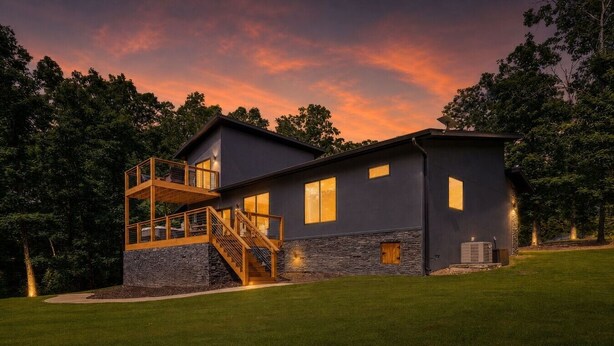 Una casa moderna de dos pisos con cimientos de piedra, una terraza de madera y una escalera que conduce a un nivel superior.