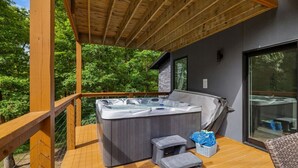 Un jacuzzi en una terraza de madera con un muro de piedra y una puerta de vidrio.