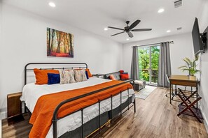 A modern bedroom with a bed, a desk, a chair, a ceiling fan, and a large window.