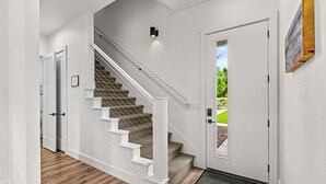 Una escalera con barandillas blancas y peldaños alfombrados que conduce a una puerta con vistas al exterior, donde se aprecia vegetación.