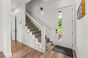 A staircase with white railings and carpeted steps leading to a door with a view of greenery outside.
