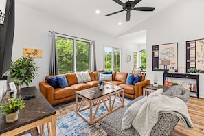 A modern living room with a brown leather sofa, a wooden coffee table, and a large window with curtains.