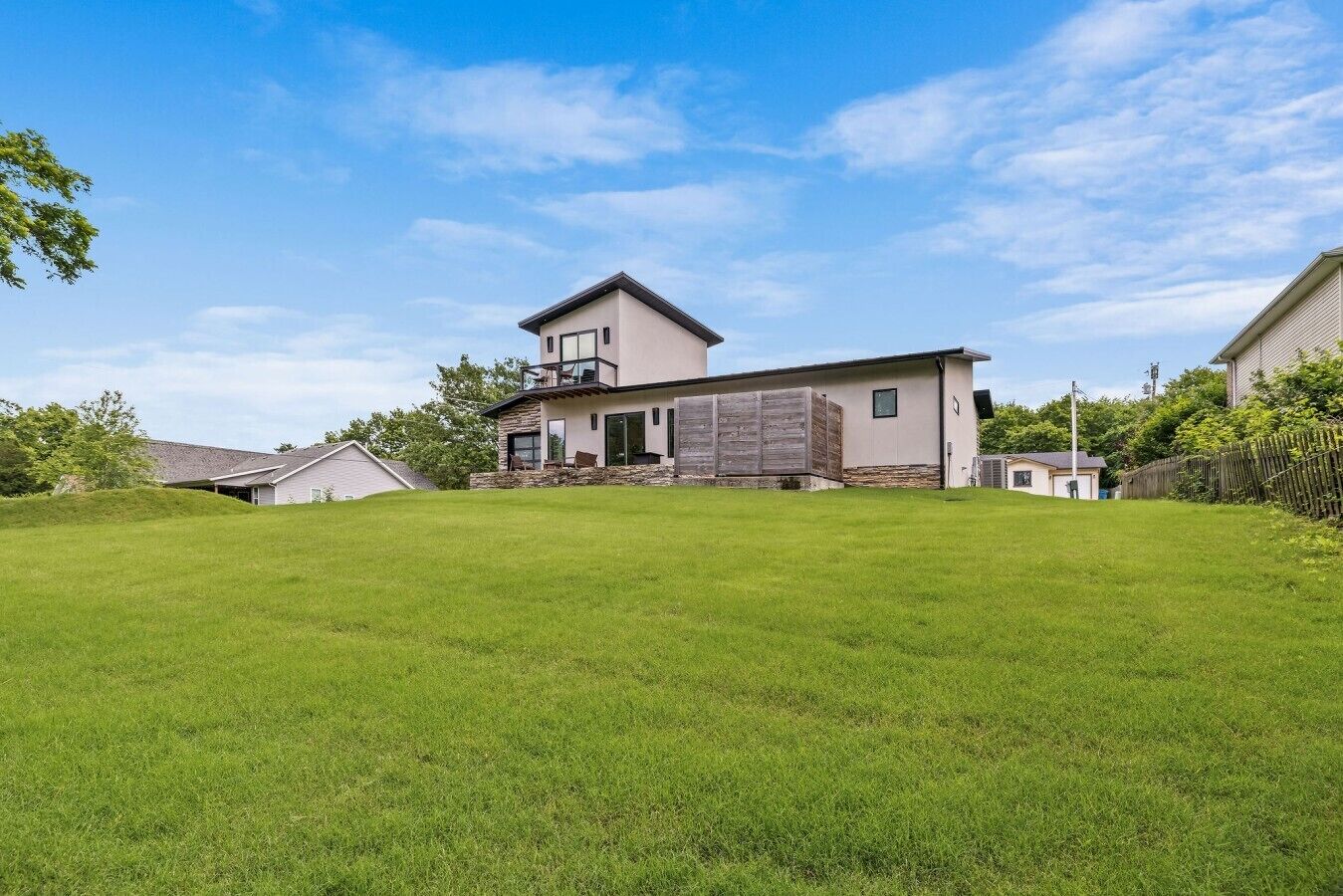 A modern two-story house with a large front yard, a balcony on the upper floor, and a garage.