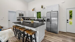 Una cocina moderna con armarios blancos, un refrigerador de acero inoxidable y una isla central con taburetes de bar.