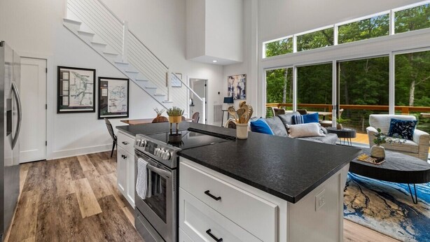 Una cocina moderna con una isla central, un comedor con vistas y una escalera que sube a un nivel superior.