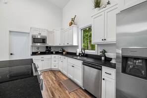 A modern kitchen with white cabinets, a stainless steel refrigerator, a built-in microwave, and a water dispenser. - Modern Chalet Near Back 40 Trails Hot Tub & Forest Views (Bella Vista)