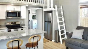 A modern kitchen with a built-in microwave, stove, and refrigerator. There is a white staircase leading to an upper level, and a gray sofa in the living area. - Mountain Views, Peaceful Backyard, King Bed, Dog Friendly (Colorado Springs)