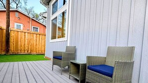 A deck with wicker furniture and a view of a house with a wooden fence and a red building in the background. - Mountain Views, Peaceful Backyard, King Bed, Dog Friendly (Colorado Springs)