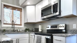 A modern kitchen with white cabinets, a stainless steel microwave, a built-in oven, and a granite countertop. - Mountain Views, Peaceful Backyard, King Bed, Dog Friendly (Colorado Springs)